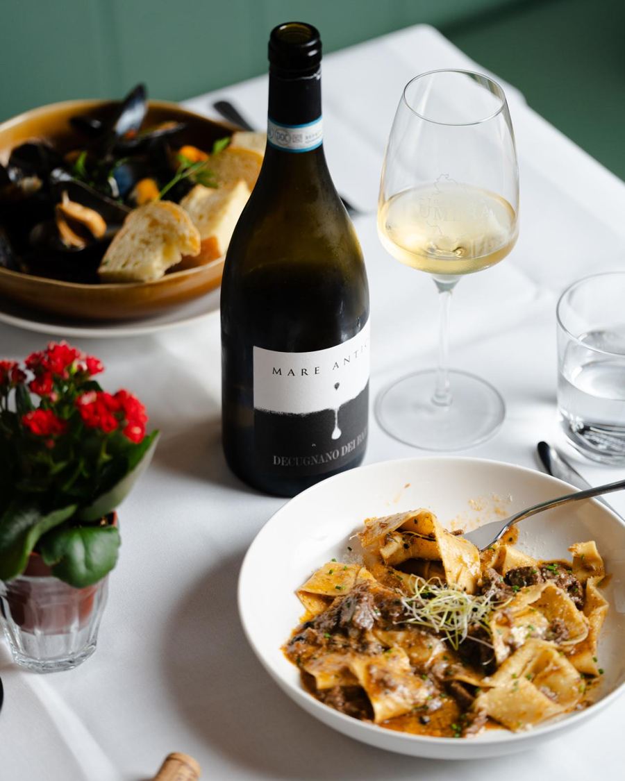 Pappardelle en een fles witte wijn op een gedekte tafel